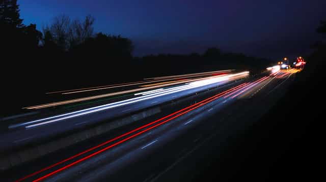 Rodovia à noite em longa exposição, com rastros de luz dos carros